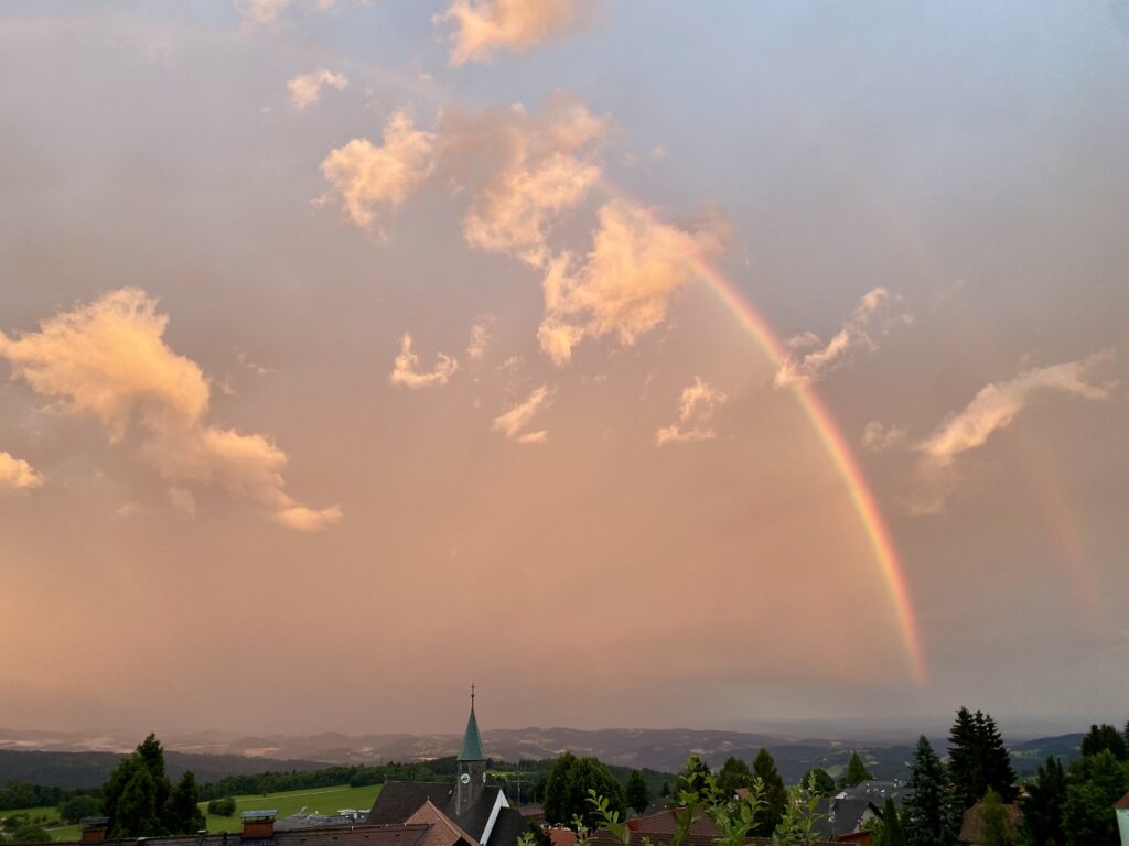 View of church, landscape and sky with clouds and rainbow.
