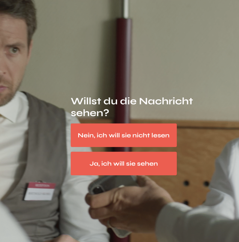 Szene in Kantine beim Mittagstisch, Blicke auf ein Handy. Frage: Willst du die Nachricht sehen? Zwei Optionen: Nein, ich will sie nicht sehen. und: Ja, ich will sie lesen.